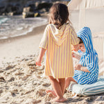 Two children on the beach wearing ponchos with a tent in the background