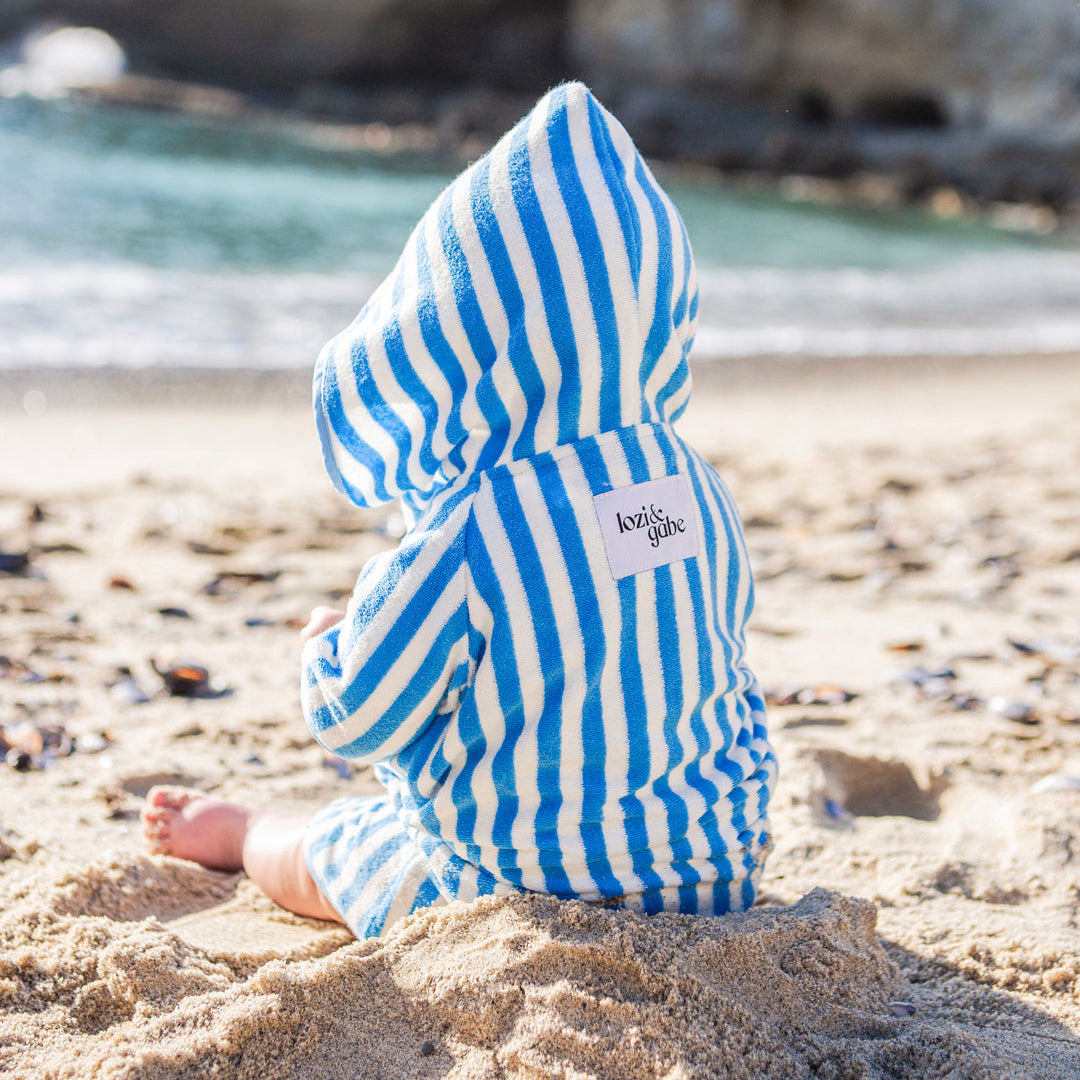 baby boy wearing blue and white striped poncho playing in the sand